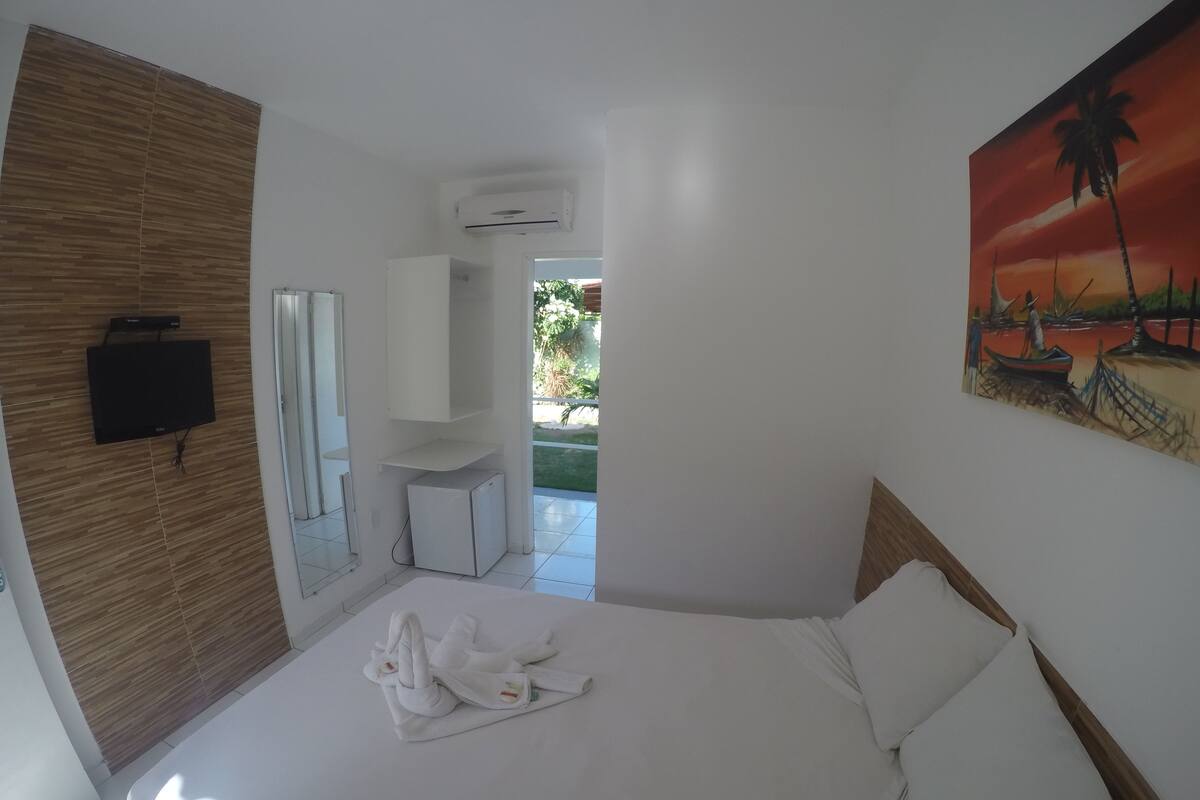 Ein Hotelzimmer mit einem Bett, einem an der Wand befestigten Flachbildfernseher, einem Sonnenuntergangsbild und einer kleinen Klimaanlage.