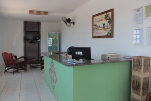 A reception area with a green counter, a television mounted on the wall, a fan, and a framed picture of a beach scene.