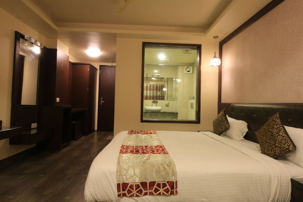 Ein Hotelzimmer mit einem großen Bett, einem Spiegel, einem Kleiderschrank und einem durch das Fenster sichtbaren Badezimmer.