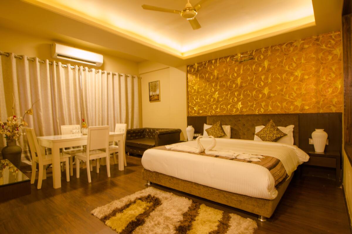 Ein Hotelzimmer mit einem großen Bett, einer Essecke mit Tisch und Stühlen, einem Deckenventilator und einer dekorativen Wandverkleidung.