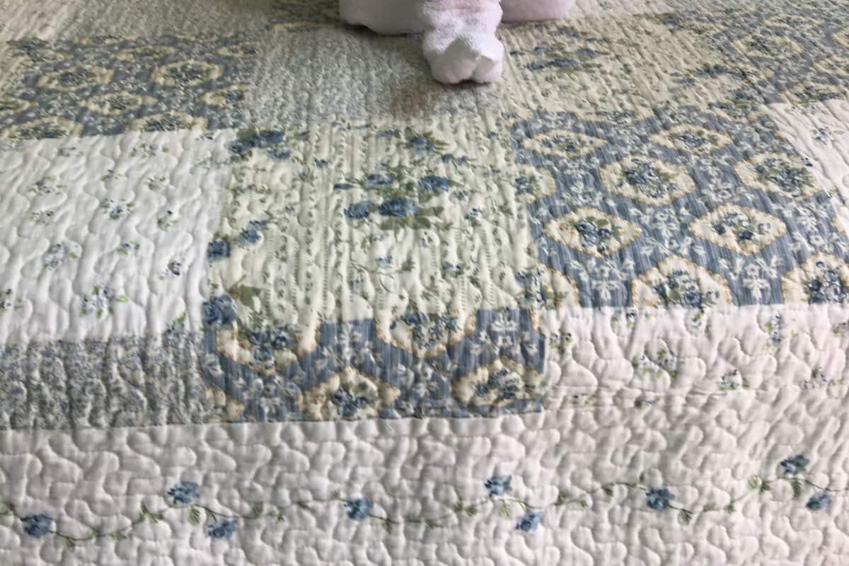 Un lit avec une couette à motifs floraux, une serviette rose et deux coussins à motifs.