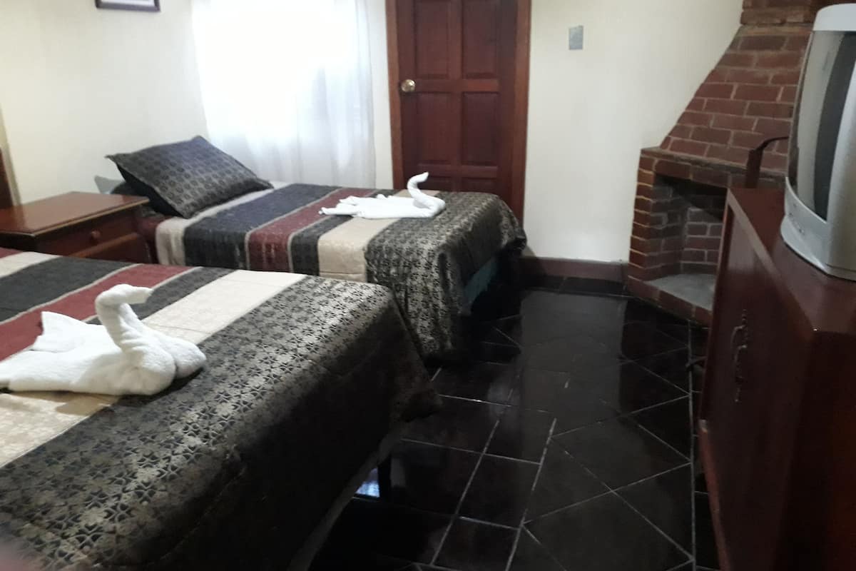 Une chambre d’hôtel avec deux lits, une télévision, une cheminée et un sol carrelé.
