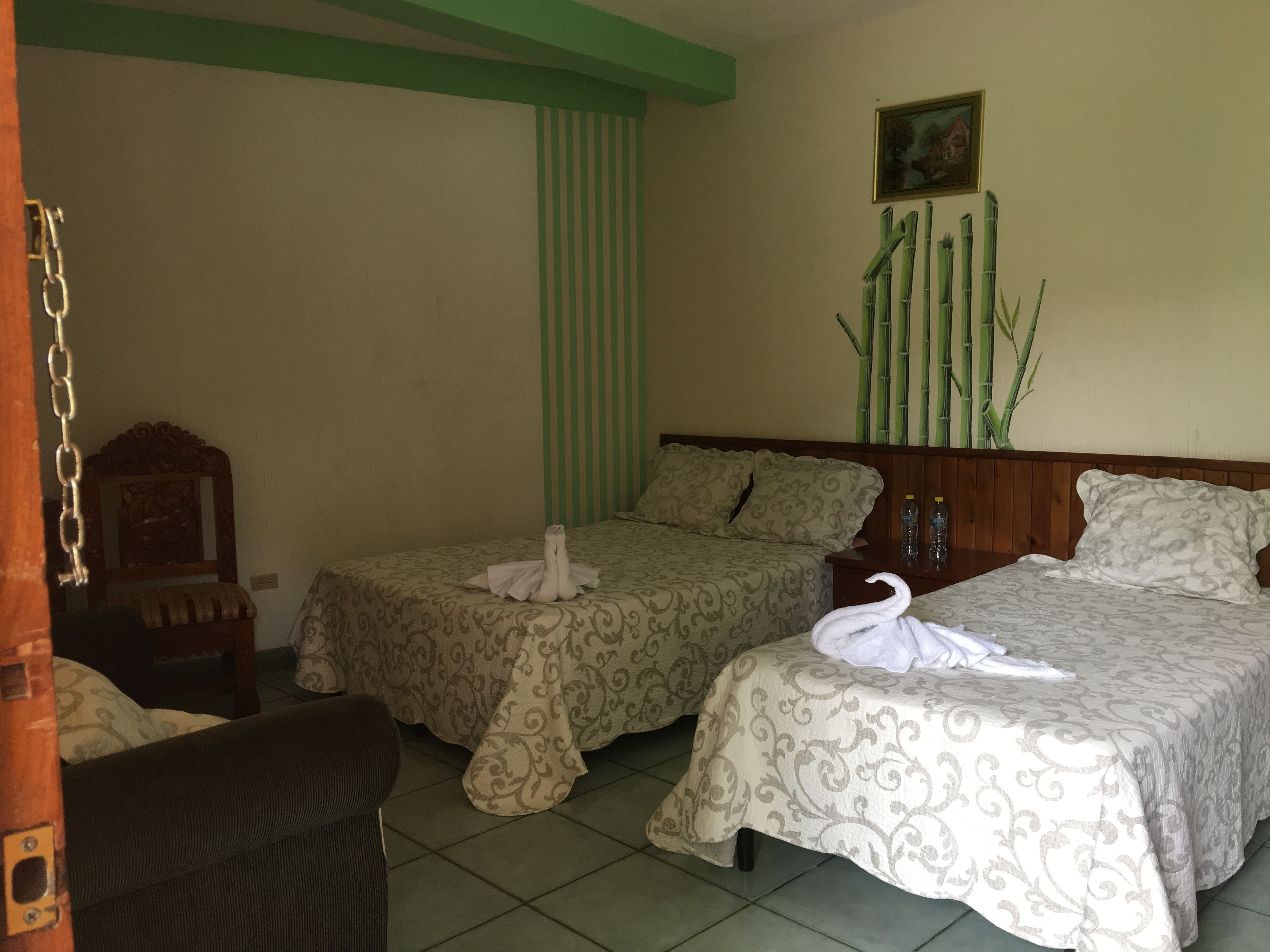 Une chambre d’hôtel avec deux lits, une tête de lit en bois, un mur à rayures vertes et une décoration en bambou.