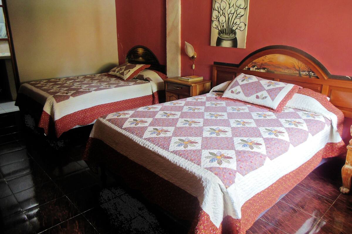 Deux lits doubles avec des couvre-lits à motifs floraux, une table de chevet avec une lampe et un tableau au mur.