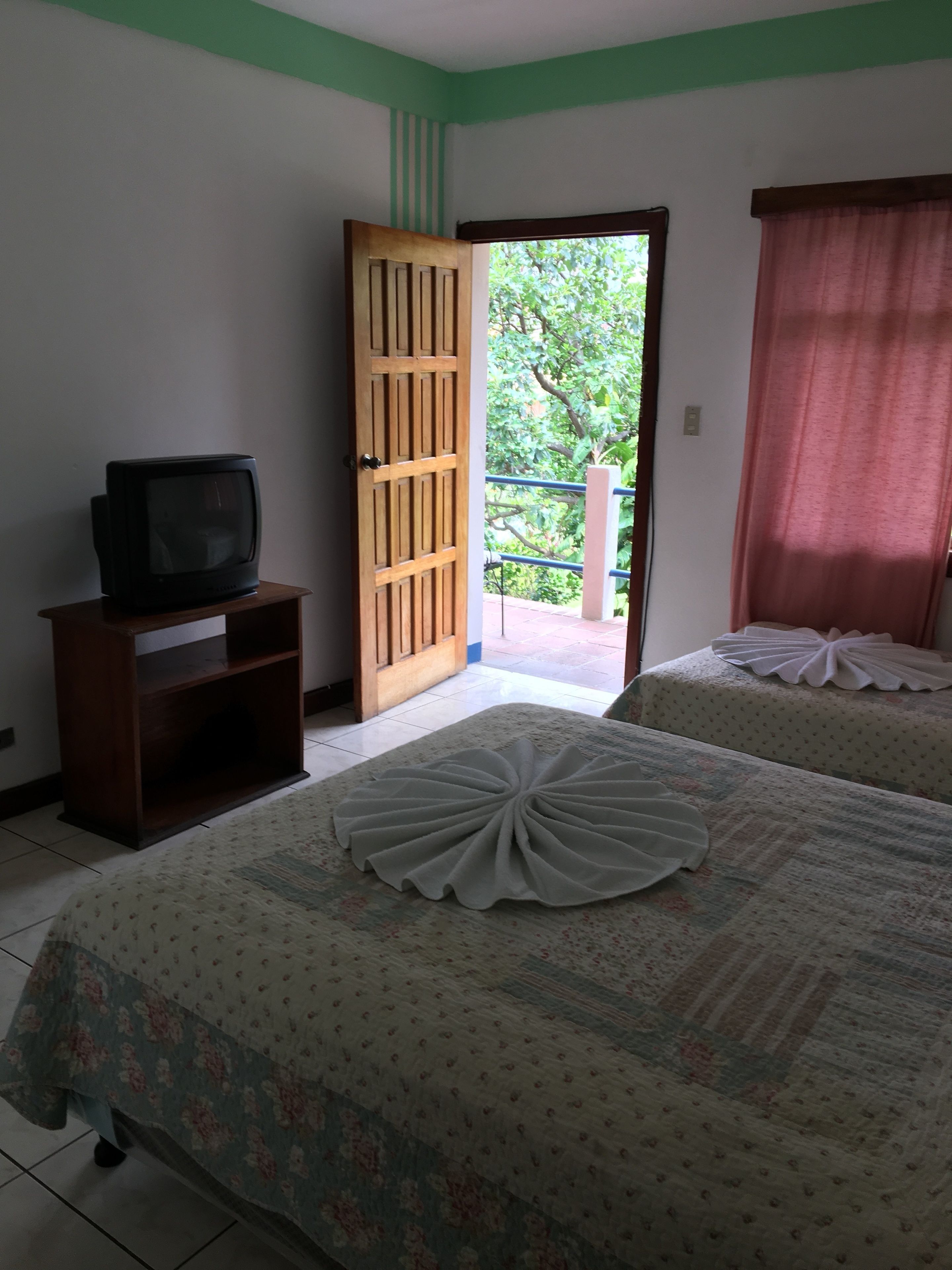 Habitación de hotel con cama, televisor sobre un soporte de madera y puerta que da a un área exterior.