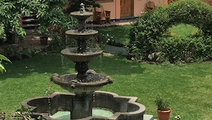Een meerlaags stenen fontein omringd door een verzorgde tuin, met een gebouw op de achtergrond.