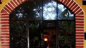 A dining area with a brick archway, a table set with a colorful tablecloth, and a view of greenery outside.