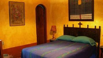 A bedroom with a bed, a nightstand, a lamp, a door, and a wall with a framed picture.