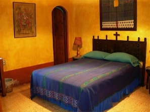 A bedroom with a bed, a nightstand, a lamp, a door, and a wall with a framed picture. - Posada Belen Museo Inn (Guatemala City)