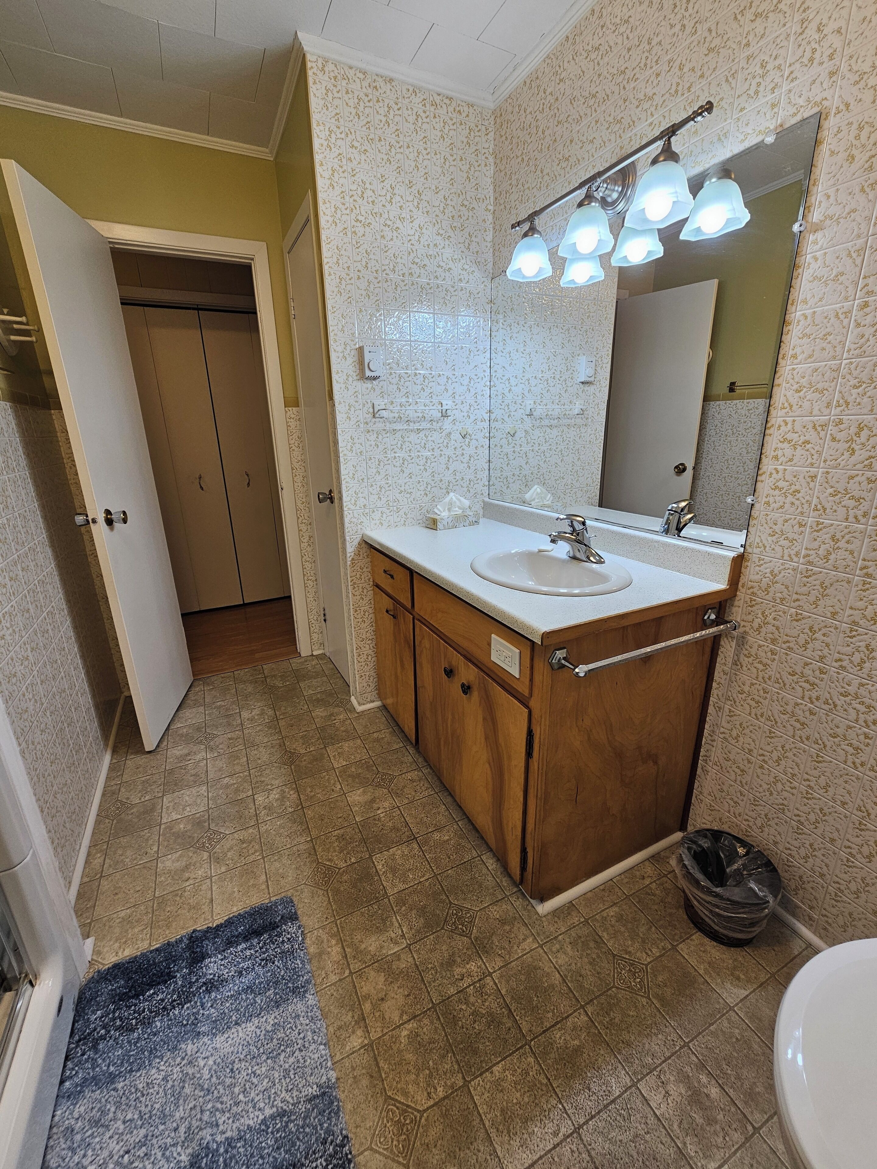 Un baño con tocador de madera, un lavamanos blanco, un espejo y una lámpara en el techo.