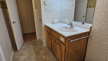 Un baño con tocador de madera, un lavamanos blanco, un espejo y una lámpara en el techo.