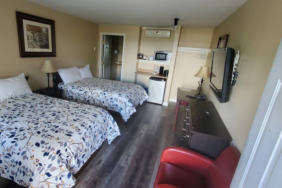 A hotel room with two beds, a desk with a microwave, a small kitchenette, and a TV.