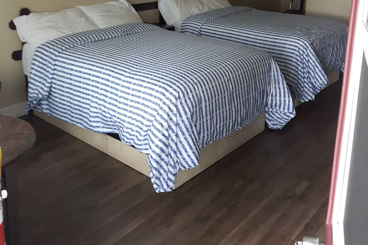 A hotel room with two beds, a nightstand, a lamp, and a framed picture on the wall.
