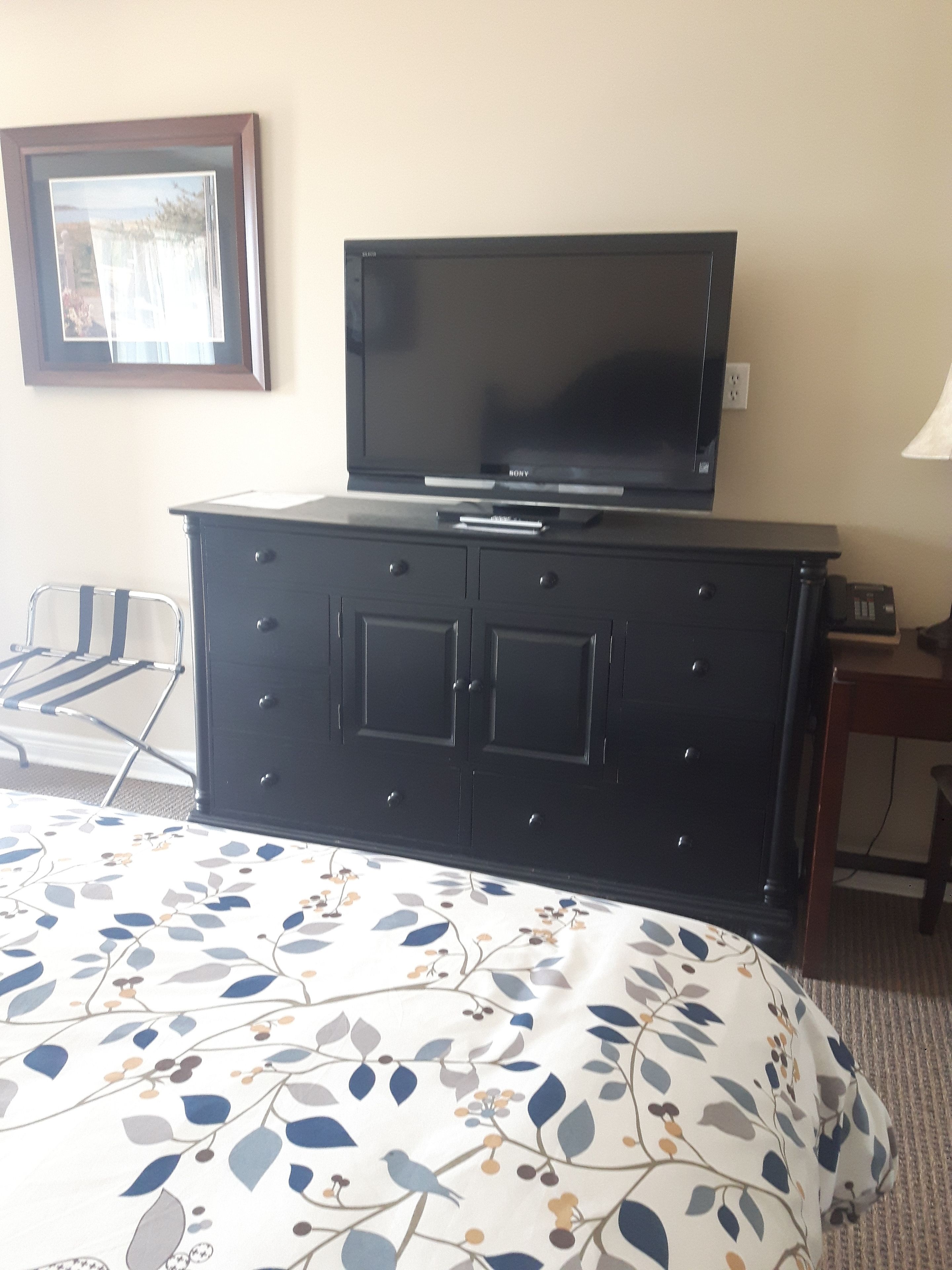 A hotel room with a bed, a dresser, a television, and a chair.