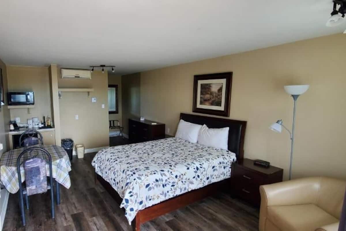 A hotel room with a bed, a desk with a chair, a television, a lamp, and a picture on the wall.