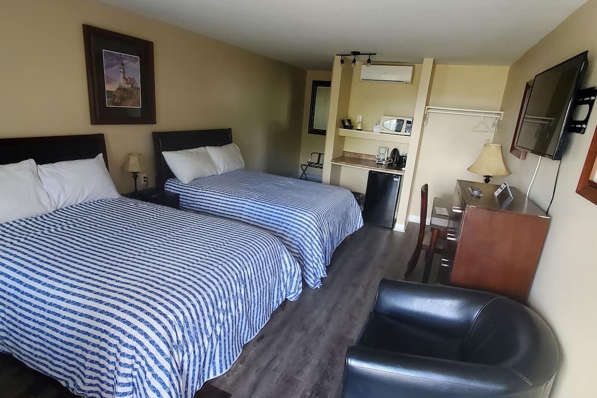 A hotel room with two beds, a desk, a chair, a TV, and a kitchenette.