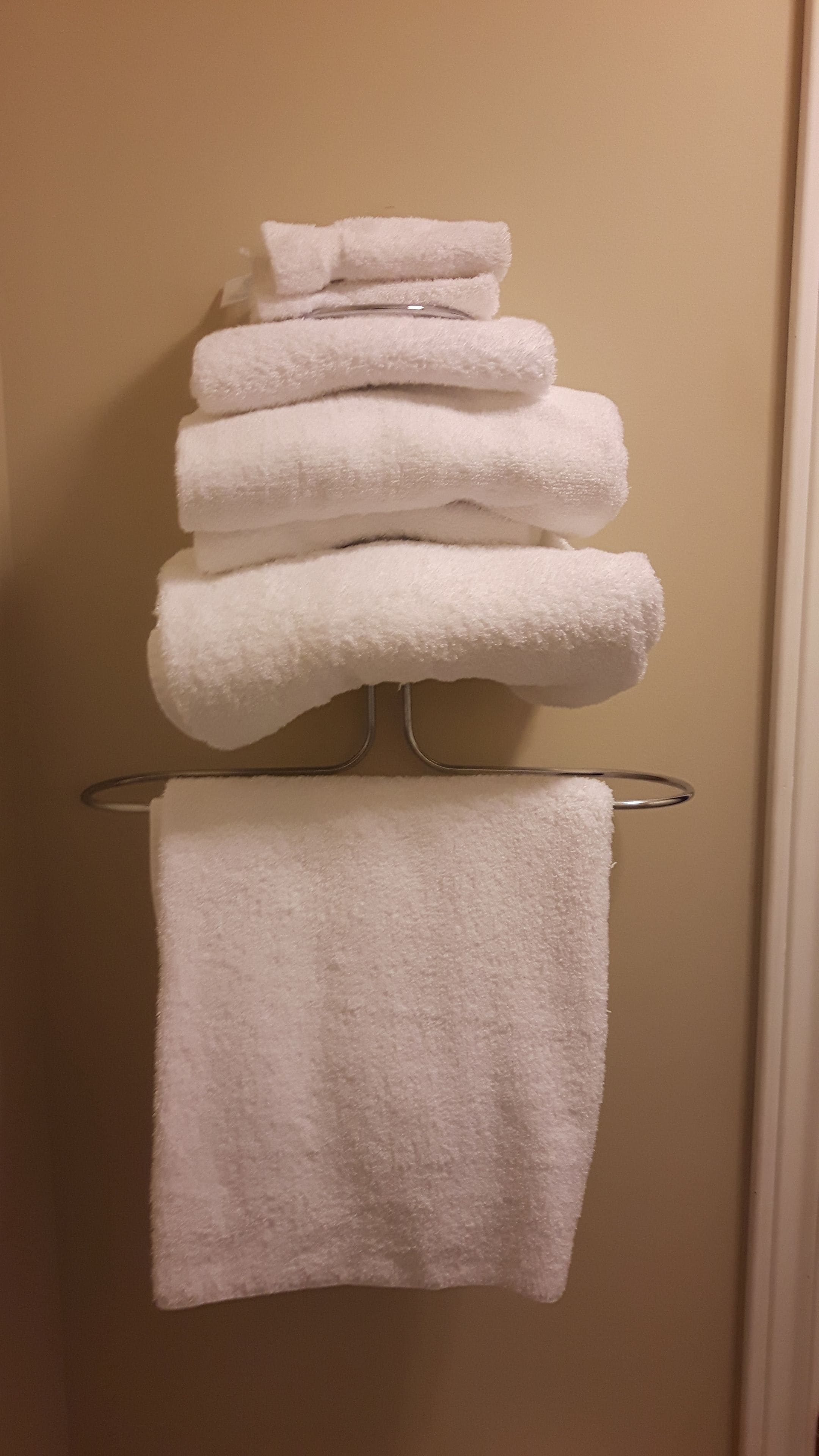 A stack of white towels on a metal towel rack against a beige wall.