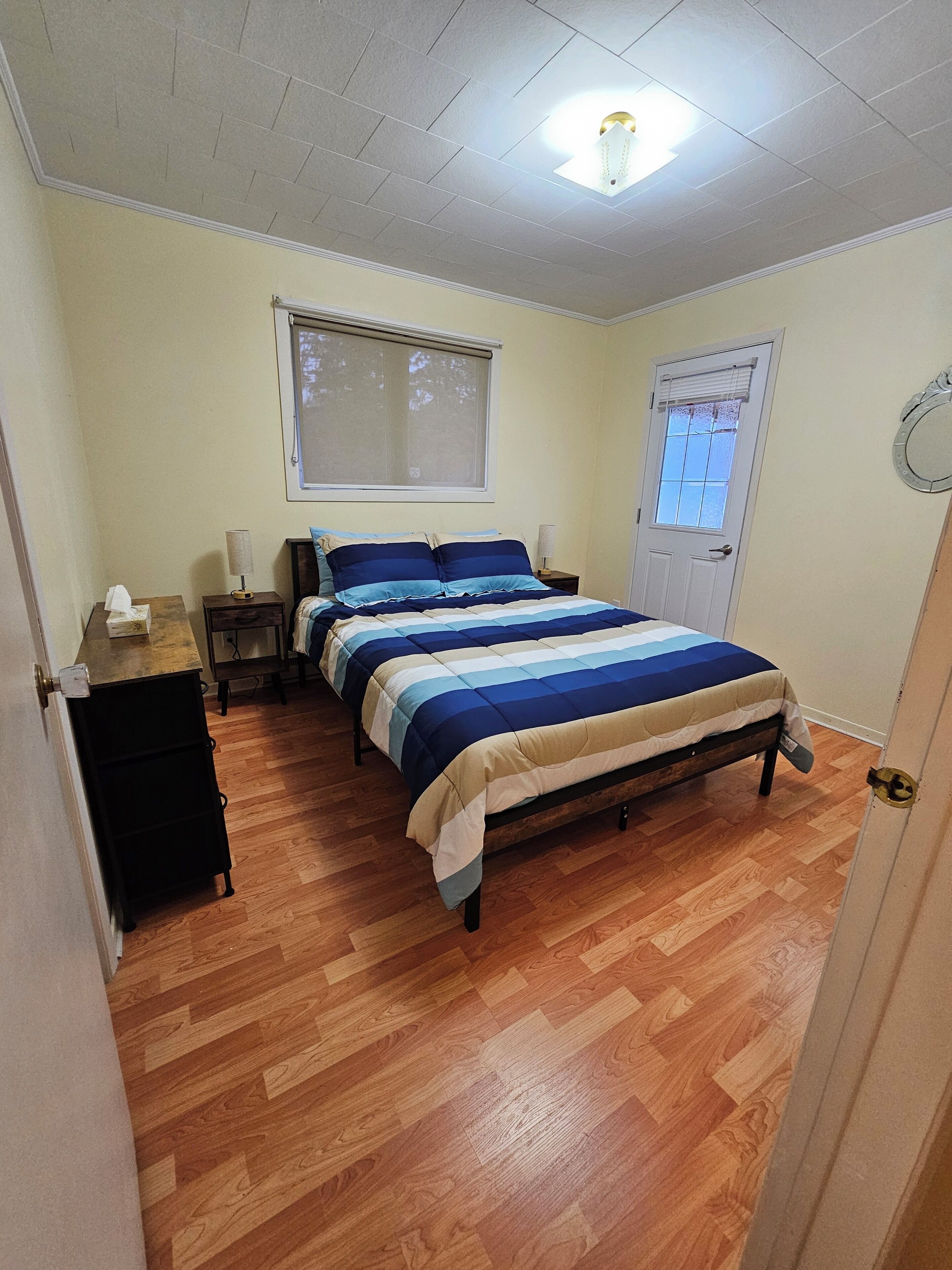 A bedroom with a bed, a nightstand, a window, and a door.