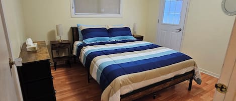 A bedroom with a bed, a nightstand, a window, and a door.
