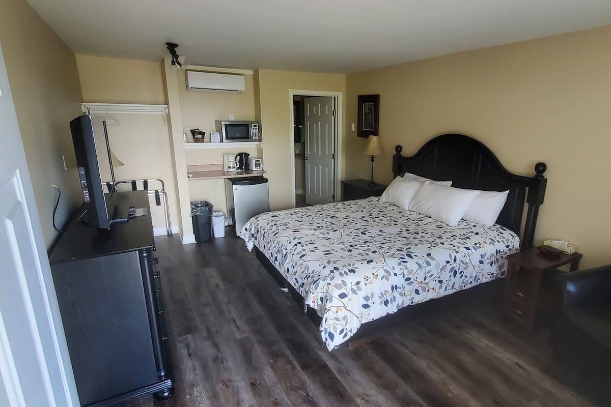 A bedroom with a bed, a dresser, a desk, a microwave, a refrigerator, and a door leading to a bathroom.