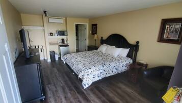 Un dormitorio con cama, cómoda, escritorio, microondas, refrigerador y puerta que da a un baño.