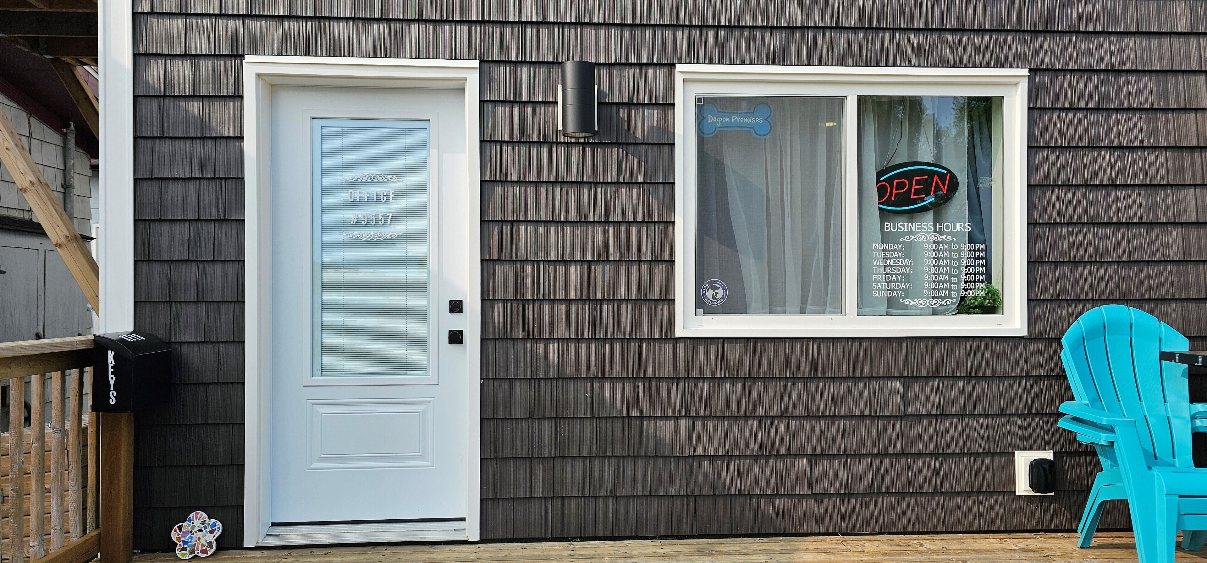 A house with a white door, a window with a 'OPEN' sign, and a blue chair outside.