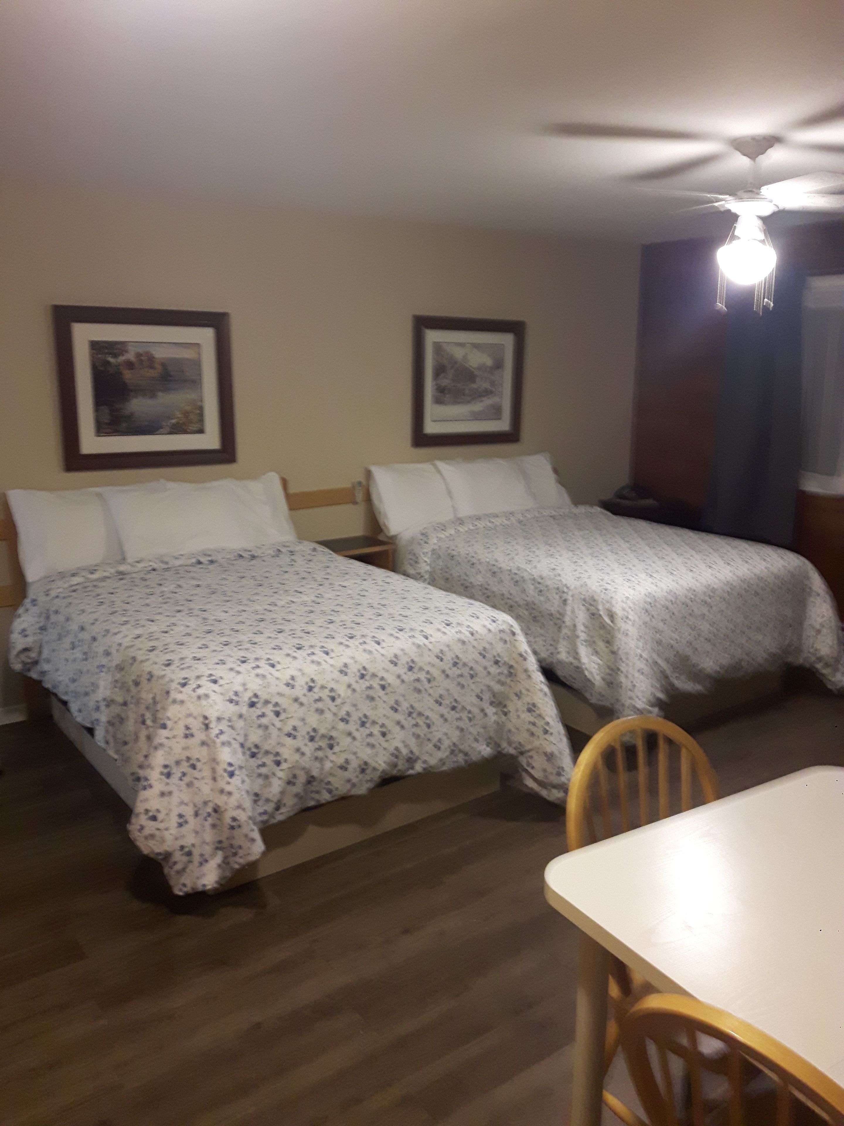 Une chambre d’hôtel avec deux lits simples, une table en bois et un ventilateur de plafond.