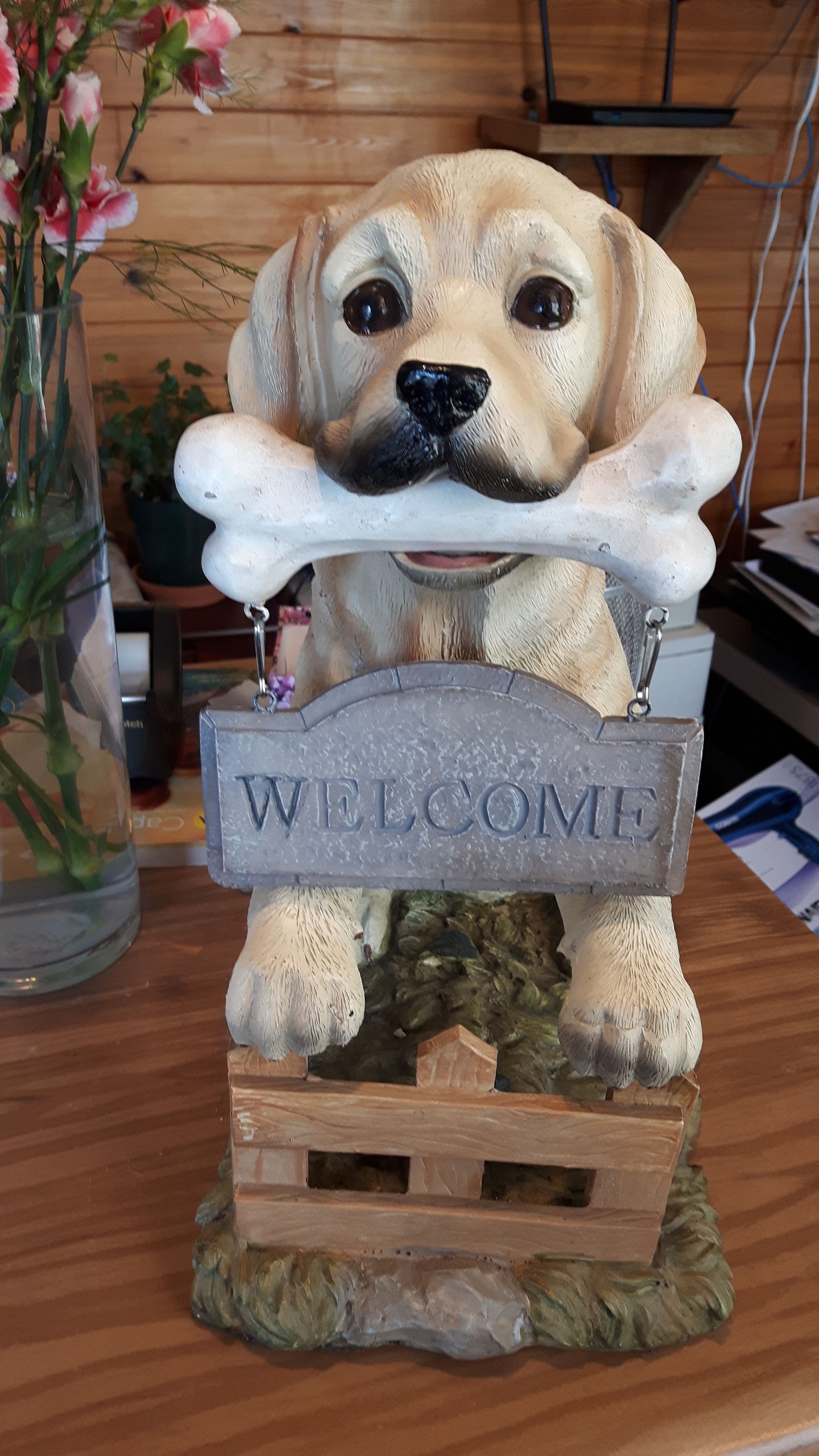 A dog figurine with a bone, sitting under a 'WELCOME' sign.