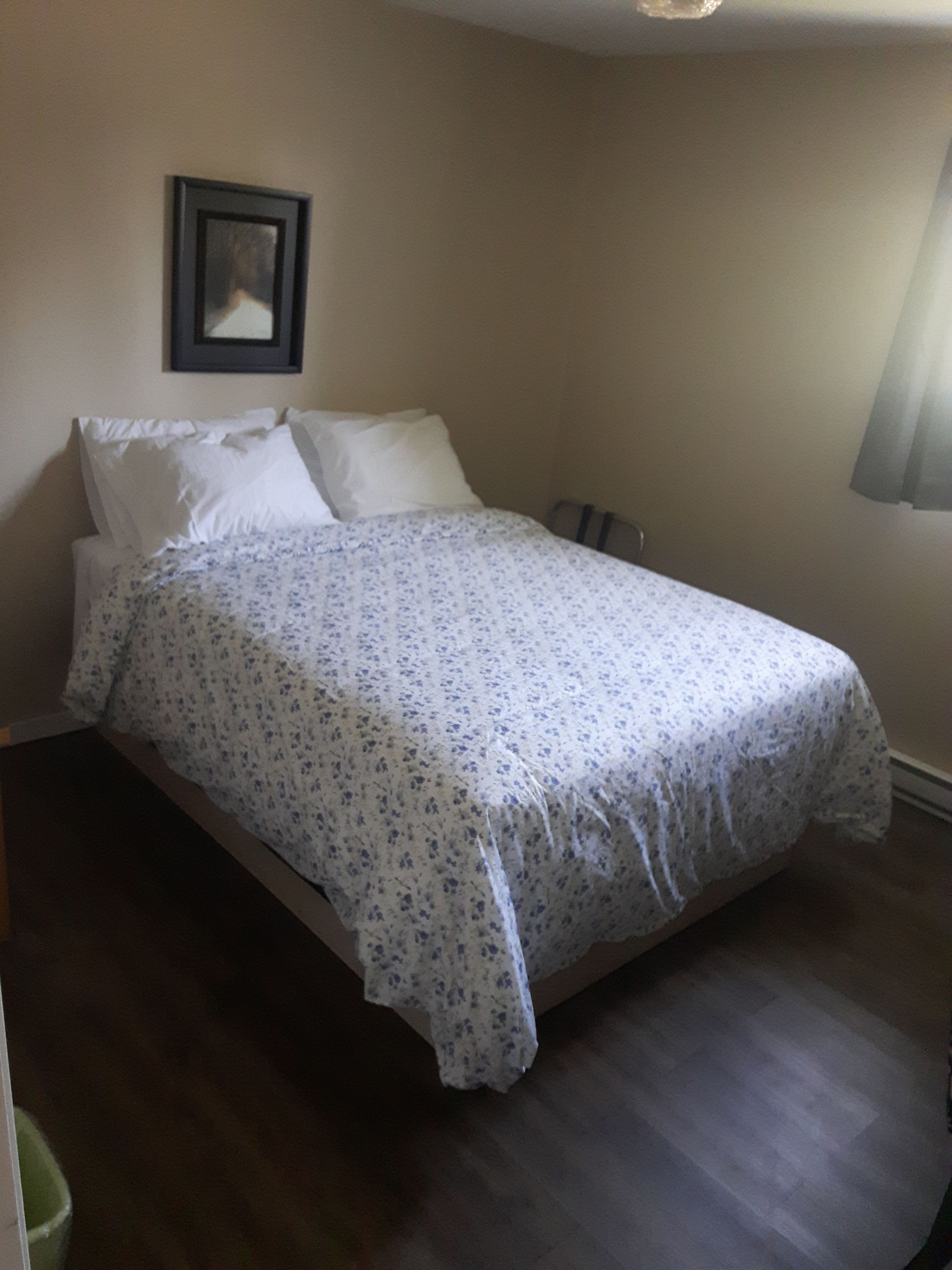 Un dormitorio con cama, ropa de cama blanca, un cuadro en la pared y una lámpara en la mesita de noche.