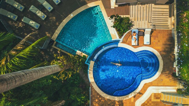 Una piscina en la azotea con diseño circular, rodeada de sillas de descanso y una palmera.