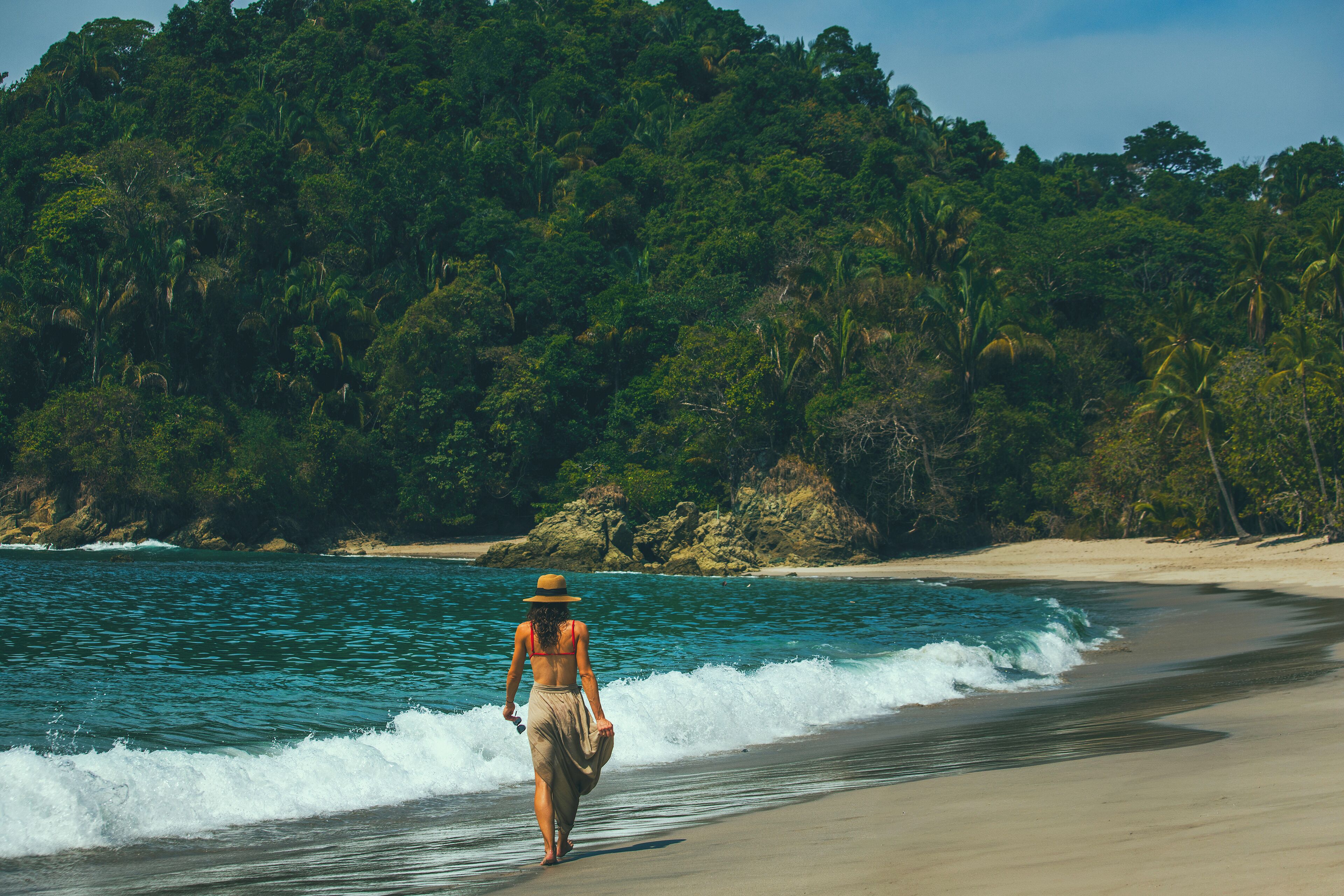 A beach with clear turquoise water, a sandy shore, and dense green foliage in the background.
