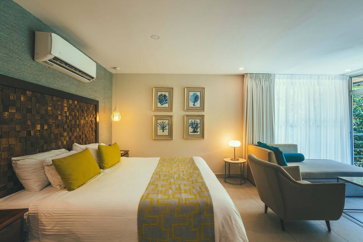 Una habitación de hotel con una cama, una silla, una mesita auxiliar y una ventana con cortinas.