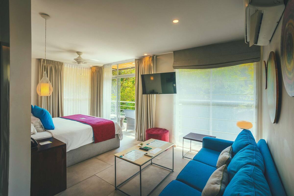 Una habitación de hotel con cama, sofá, televisión y ventana con cortinas.