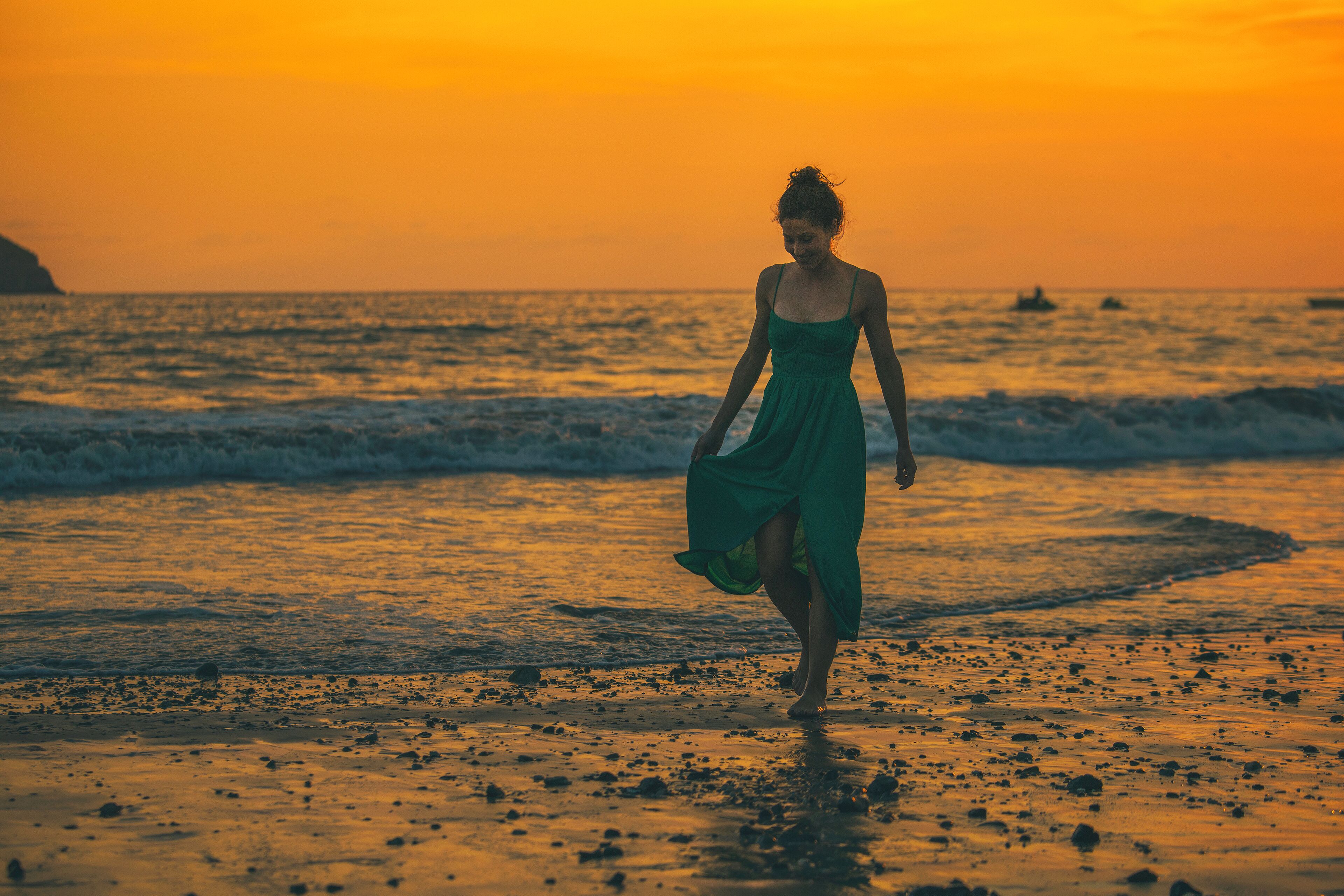 A woman in a green dress walking on a beach at sunset.