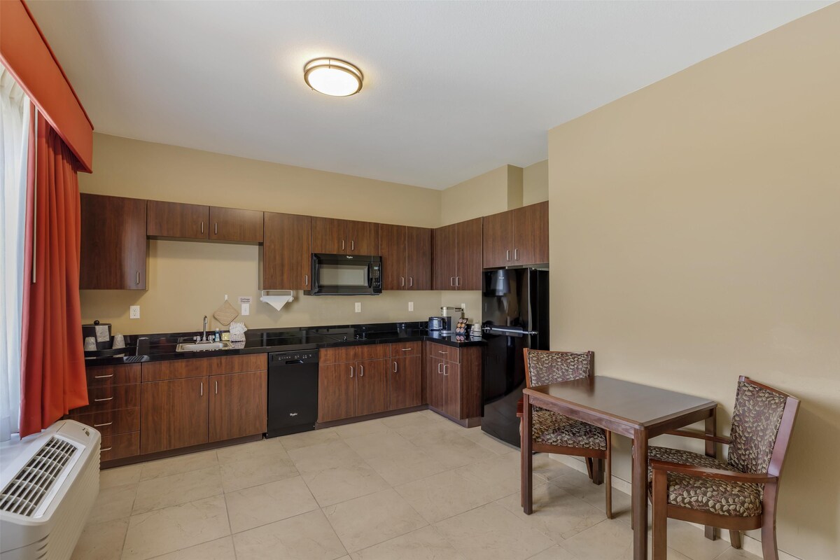 A compact kitchen with wooden cabinets, a microwave, and a refrigerator. There is a dining table with two chairs.