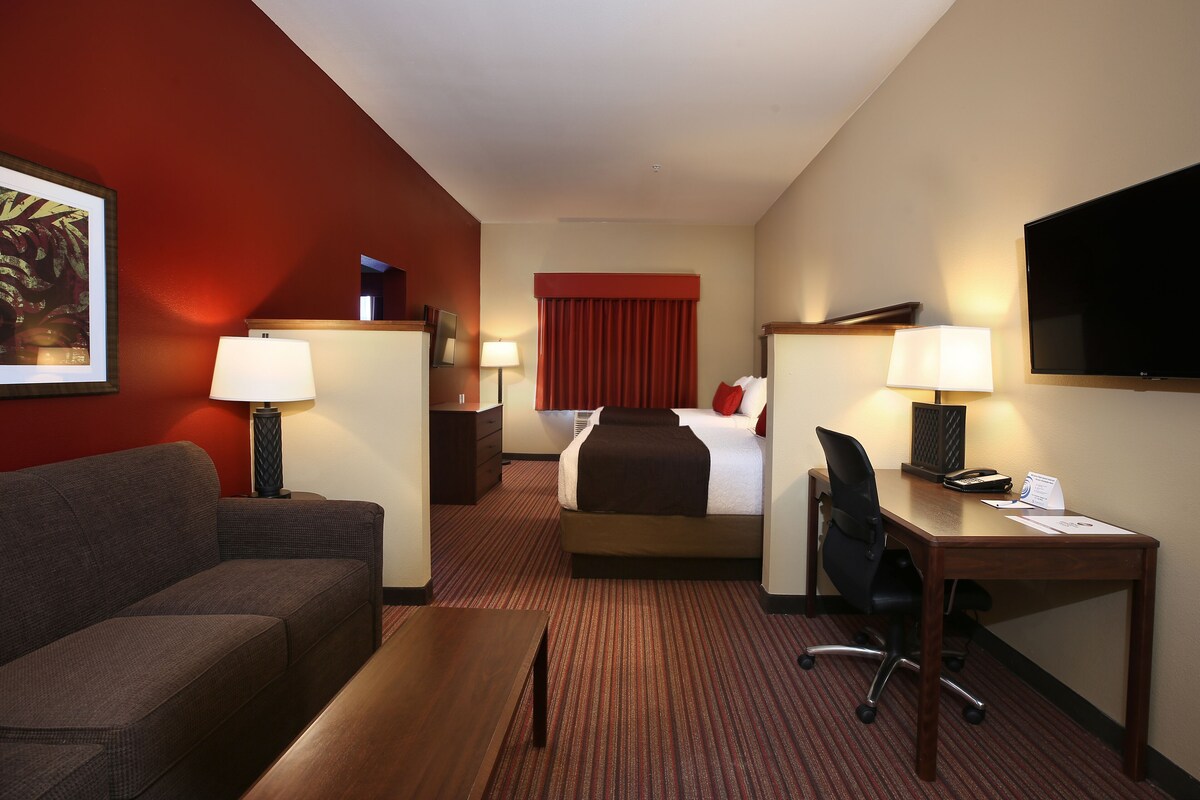 A hotel room with a bed, a desk, a chair, a sofa, and two lamps.