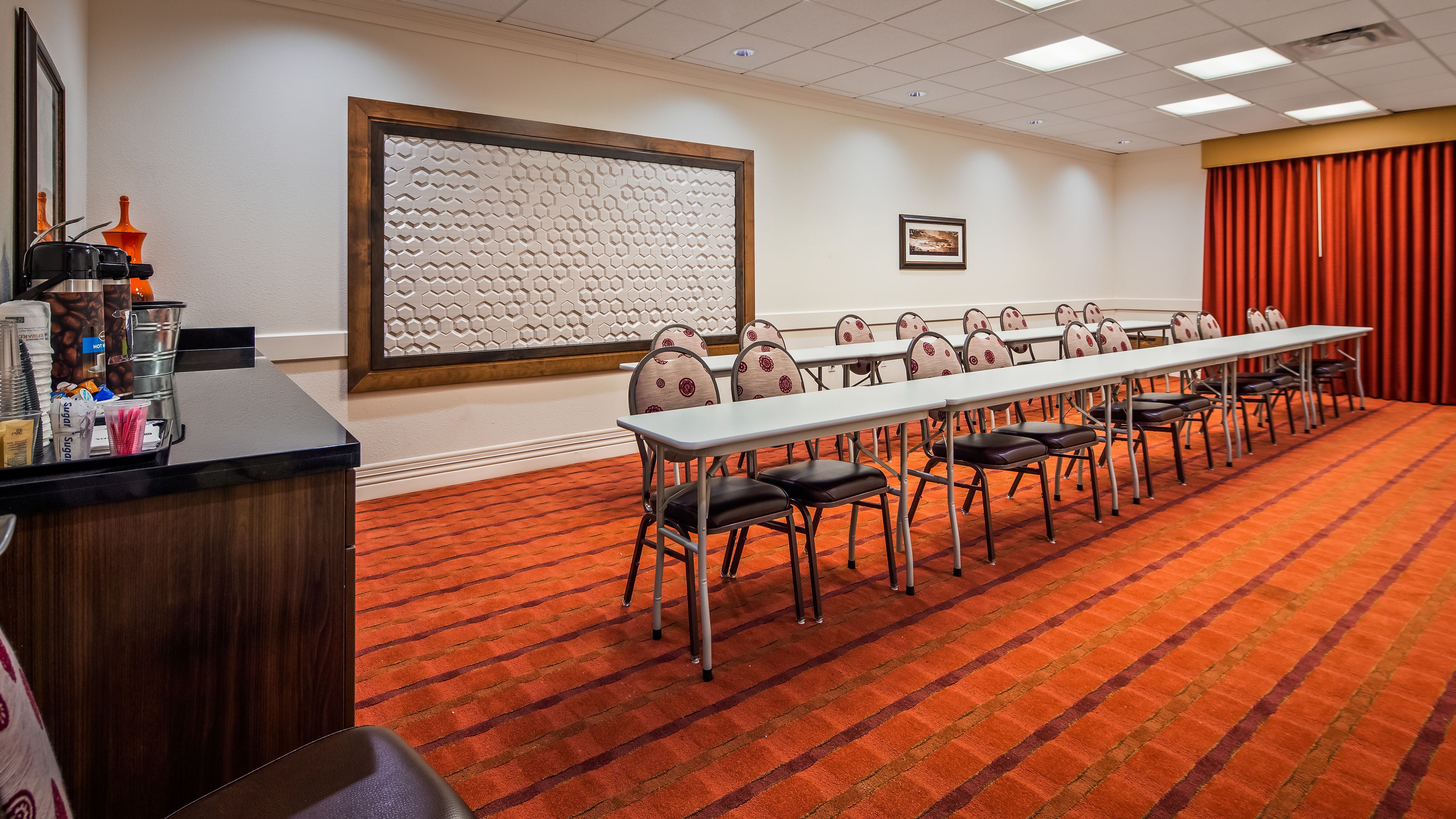 A conference room with a long table, chairs, a projector screen, and a coffee station.