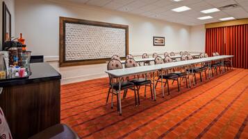 A conference room with a long table, chairs, a projector screen, and a coffee station.