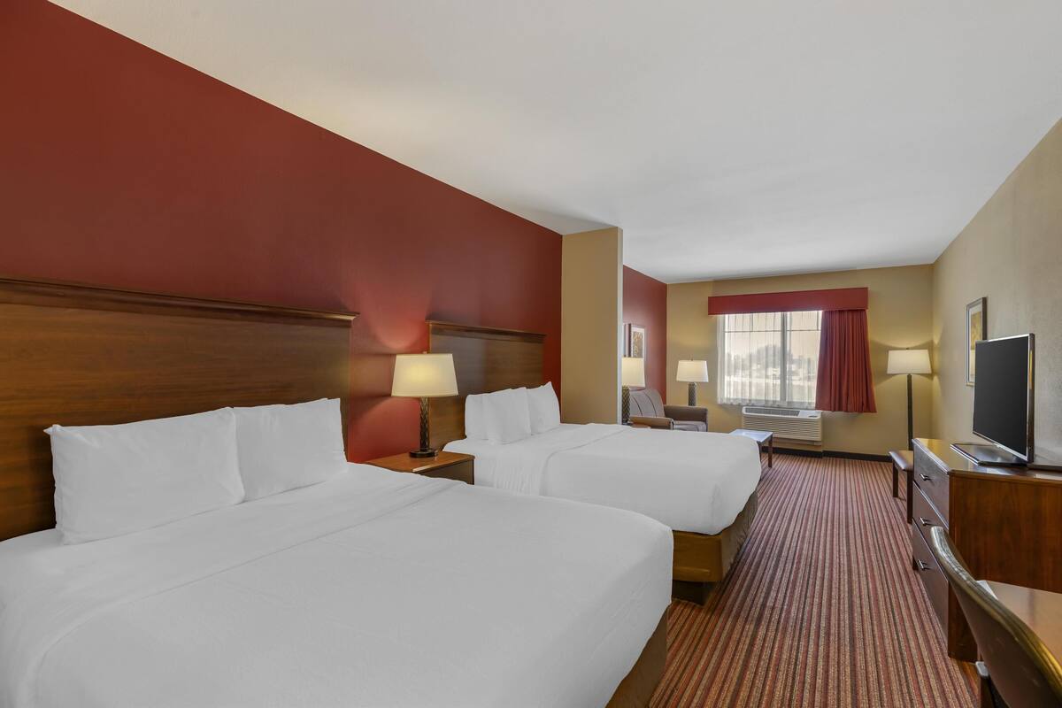 A hotel room with two beds, a desk, a TV, and a window with curtains.