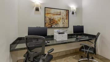 A modern office space with two desks, chairs, a large painting, and two wall-mounted lamps.