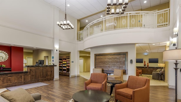 A spacious lobby with a high ceiling, a reception desk, seating area, and a kitchen in the background. - Best Western Plus Hudson Hotel & Suites (Hudson)