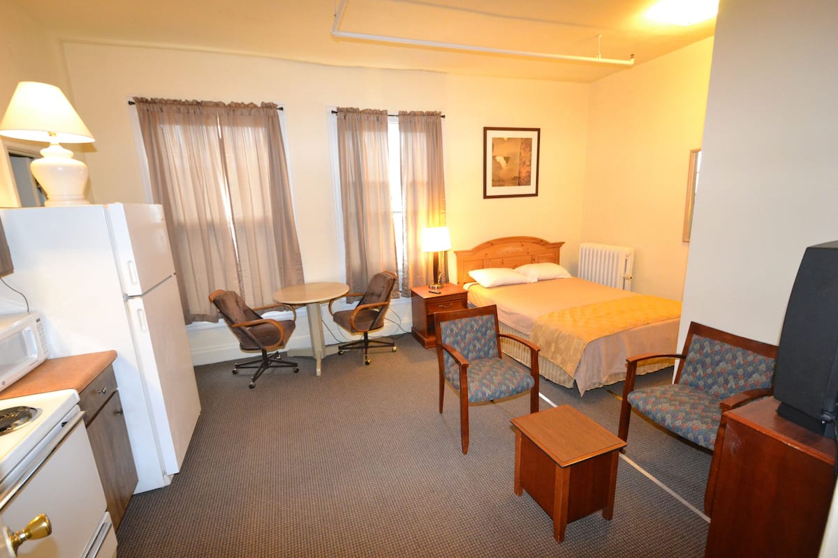 A hotel room with a bed, two chairs, a small table, a lamp, a television, a refrigerator, and a microwave.