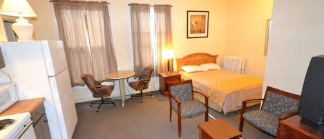 A hotel room with a bed, two chairs, a small table, a lamp, a television, a refrigerator, and a microwave.