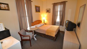 A hotel room with a bed, a desk with a chair, a television, and a window with curtains. - Perfect Stay Inn & Suites (Blair)