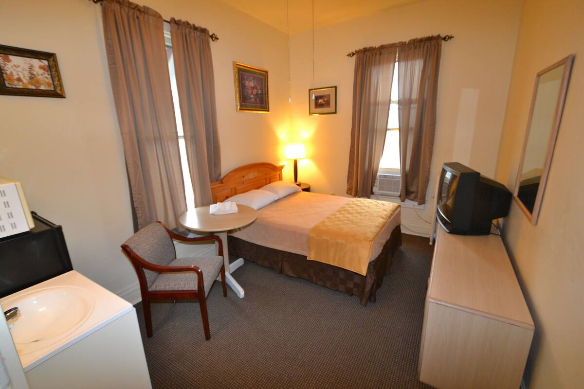 A hotel room with a bed, a desk with a chair, a television, and a window with curtains.