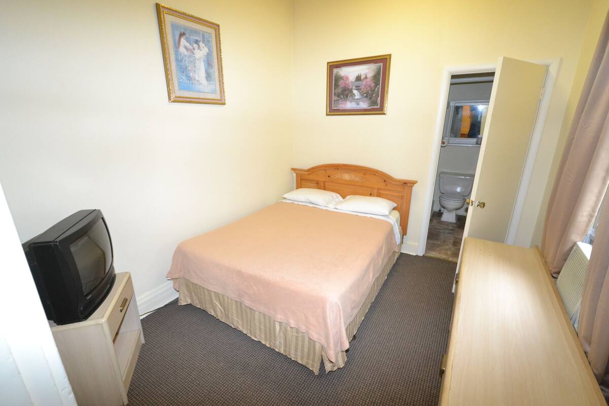 A hotel room with a bed, a television, a dresser, and a bathroom visible through an open door.