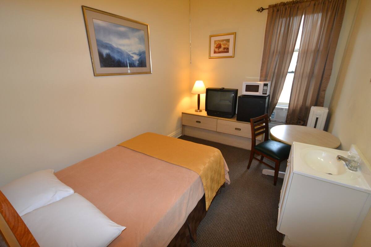 A hotel room with a bed, a desk with a chair, a television, a microwave, and a sink.