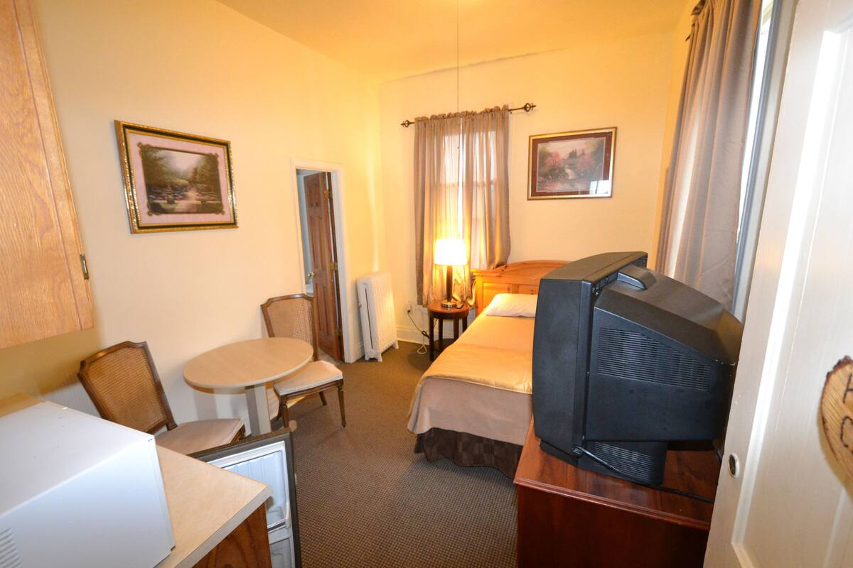 A hotel room with a bed, a television, a table with a chair, a lamp, and two framed pictures on the wall.