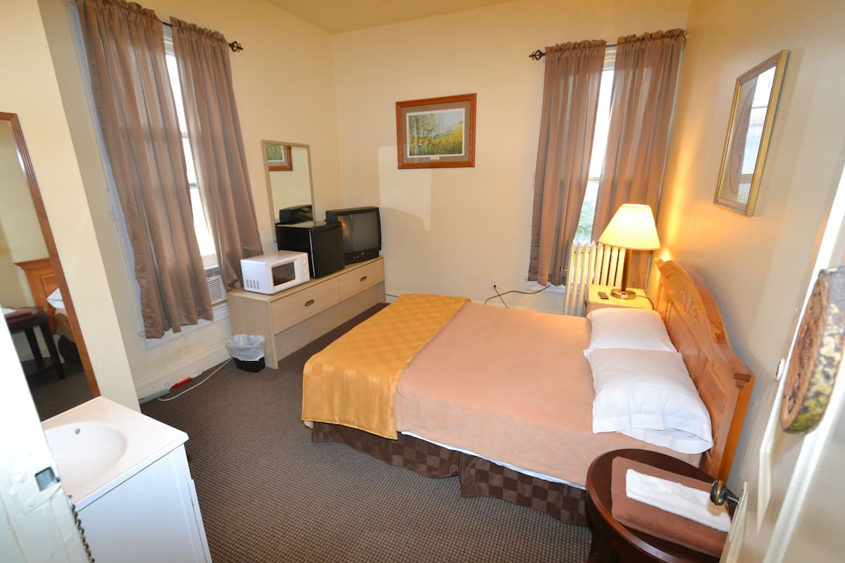 A hotel room with a bed, a desk with a computer, a lamp, a mirror, and a window with curtains.