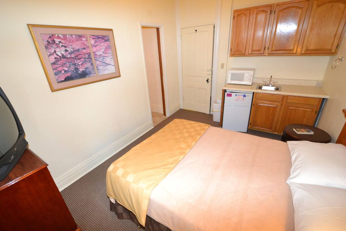 A hotel room with a bed, a television on a wooden stand, a microwave, and a small kitchenette.